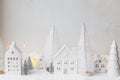 Cozy christmas miniature village. Stylish little ceramic houses and trees on snow blanket with golden lights on white background. Royalty Free Stock Photo