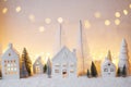 Cozy christmas white miniature village. Stylish little ceramic houses and trees on snow blanket with golden lights in evening. Royalty Free Stock Photo