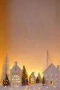 Cozy christmas white miniature village. Stylish little ceramic houses and trees on snow blanket with golden lights in evening. Royalty Free Stock Photo