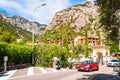 Cozy city street of Limone Sul Garda city with driving cars, tourists, hotels, small businesses with high dolomite mountains on