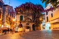 Cozy city streets in Sirmione. Vibrant violet purple flowers growing on facade of medieval building in Old Town. People walking by