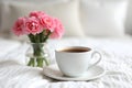 cozy Coffee cup and pink carnations in vase on white bed background Royalty Free Stock Photo
