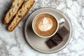 A cozy coffee setup featuring latte art, chocolate, and biscotti on a marble surface Royalty Free Stock Photo