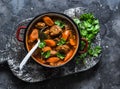 Cozy comfort winter autumn food - spicy braised crock pot beef in a pot on a rustic wooden board on a dark background, top view