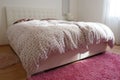Cozy compact bedroom with white furniture, pink carpet and tulle curtains. Fluffy feather blanket is thrown over the bed Royalty Free Stock Photo