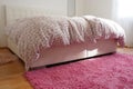 Cozy compact bedroom with white furniture, pink carpet and tulle curtains. Fluffy feather blanket is thrown over the bed Royalty Free Stock Photo