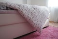 Cozy compact bedroom, white furniture, pink carpet and tulle curtains. Fluffy feather blanket thrown over the double bed Royalty Free Stock Photo