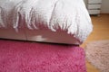 Cozy compact bedroom, white furniture, pink carpet and tulle curtains. Fluffy feather blanket thrown over the double bed Royalty Free Stock Photo