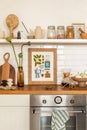 Cozy composition of kitchen interior with mock up poster frame, vase with flowers, white tile, wooden countertop, jar with spices