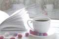 Cozy concept: a white cup of coffee stands on a white wooden table next to a white open book and colorful candy against the Royalty Free Stock Photo