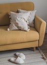 A cozy corner of the living room - a yellow sofa with decorative pillows, furry white slippers on the carpet Royalty Free Stock Photo