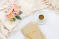 Cozy cream blanket on white bed with espresso, notebooks, and flowers