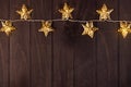 Cozy dark Christmas background with golden stars on glowing garland on brown wooden table as festive border, top view. Royalty Free Stock Photo