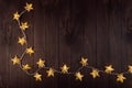 Cozy dark christmas background with golden stars on glowing garland on brown wooden table as festive frame, top view. Royalty Free Stock Photo