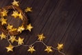 Cozy dark Christmas background with golden wreath, stars on glowing garland on brown wooden table as festive border, top view. Royalty Free Stock Photo