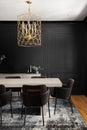 A black dining room with wainscoting walls and gold chandelier.