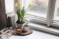 Cozy Easter spring still life scene. Cup of coffee, sweet bun, books, wooden cutting board, milk pitcher and vase of