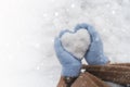 Cozy female hands in blue fluffy mitten with heart of snow in winter day. Love concept. Snow falls. Valentine day background. Copy