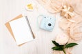 Cozy feminine home office desk. Modern instant camera, beige scarf, peonies flowers, paper notepad. Top view, tender minimal flat