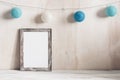 Cozy festive minimalist home decor. Blank portrait frame mockup and blue balls garland. A white wooden old table and a shabby