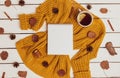 Cozy flat lay of notepad, cups of lemon tea, yellow sweater, leaves, cinnamon sticks and pine cones on white wooden background.