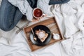 Cozy flatlay of bed with wooden tray with pie, ice cream and black tea and woman`s hands