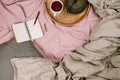 Cozy flatlay of woman`s bed with pink sheets and linen grey blanket with tray and notebook