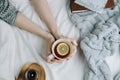 Cozy flatlay of woman`s hand holding lemon tea in bed with white sheets and blanket