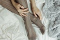 Cozy flatlay of woman`s legs in warm grey stockings in bed with knitted sweater and blanket aside Royalty Free Stock Photo