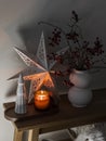 Cozy home Christmas atmosphere - cranberry branches in a vase, a paper Christmas star, a burning candle on a wooden background