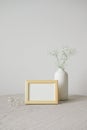 Cozy home desk with picture frame mockup and vase of flowers. White wall on background. Hygge, nordic style room interior decor Royalty Free Stock Photo