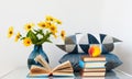 Cozy home interior decor: stack of books, peach, decorative pillows and vase with yellow flowers on a table. Distance home Royalty Free Stock Photo