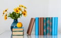 Cozy home interior decor: stack of books, peach and vase with yellow flowers on a table. Distance home education.Quarantine Royalty Free Stock Photo