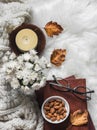 Cozy home interior - stack of books, almond nuts, knitted plaid, candle, chrysanthemum bouquet, fur carpet on a light background,