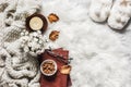 Cozy home interior - stack of books, almond nuts, knitted plaid, candle, chrysanthemum bouquet, fur carpet, soft slippers on a