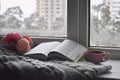 Cozy home still life: cup of hot coffee, spring flowers and opened book with warm plaid on windowsill against snow