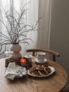 A cozy homemade breakfast is served on a table with dishes, cups, lighted candles and a plate of pancakes on a wooden table