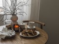 A cozy homemade breakfast is served on a table with dishes, cups, lighted candles and a plate of pancakes on a wooden table