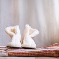 Cozy homemade white boots made of faux fur on a striped woolen plaid on a beige background