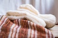 Cozy homemade white boots made of faux fur with a striped woolen plaid on a beige background