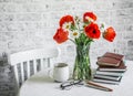 Cozy interior home concept. Bouquet of poppies, daisies, stack of books, cup of tea on a table in a light room