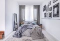 Cozy king size bed with grey bedding and warm blanket in elegant bedroom interior with mirror and photos on the wall Royalty Free Stock Photo