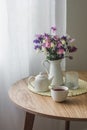 Cozy kitchen interior - a jug with summer garden flowers, a cup of tea, a teapot on a round wooden table Royalty Free Stock Photo