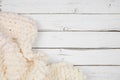 Cozy cream colored knitted thick wool blanket, top view corner border on a white wood background