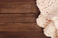 Cozy cream colored knitted thick wool blanket, top view side border on a rustic dark wood background