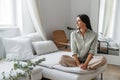 In cozy living room happy woman sitting in lotus position leaning on sofa, 30s european woman enjoying lazy weekend or