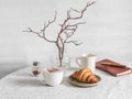 Cozy morning - cappuccino, croissant, vase with branches, leather planner notebook on the table in a bright cozy room. Cozy home