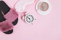 Cozy morning at home. Coffee, sleeping mask, slippers and alarm clock on pink background