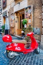 Cozy narrow ancient medieval Old Town paving stone street with coffee bars, small businesses, parked red vintage mopeds in Rome,