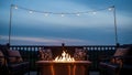 Cozy outdoor evening setting features a lit gas fire pit surrounded by comfortable patio seating under decorative string lights Royalty Free Stock Photo